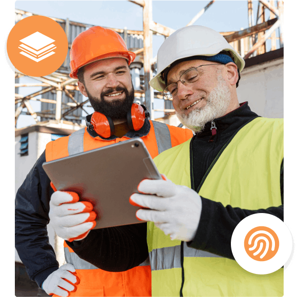 Two construction workers smiling while looking at a tablet.