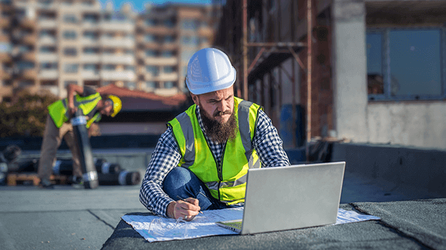 A construction worker on a construction site looking at a laptop.